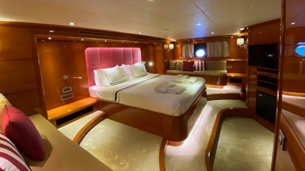 Вид сбоку на спальняю  гулеты Gül Maria с большой кроватью с розовым изголовьем  и диванами с подушками